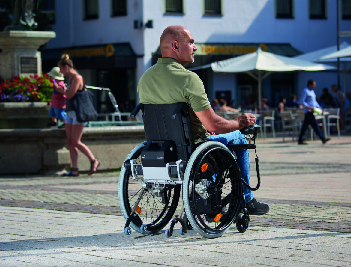 Muž na elektrickém invalidním vozíku na městském náměstí při jarním a letním pohybu venku